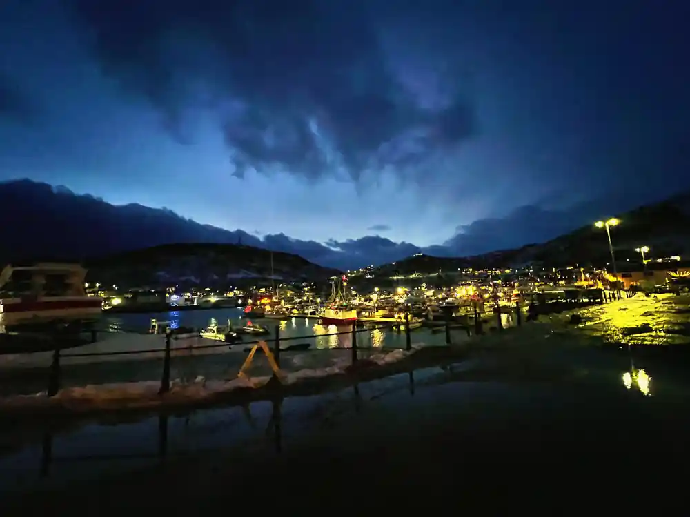 A lit coastal town at night below dark mountains
