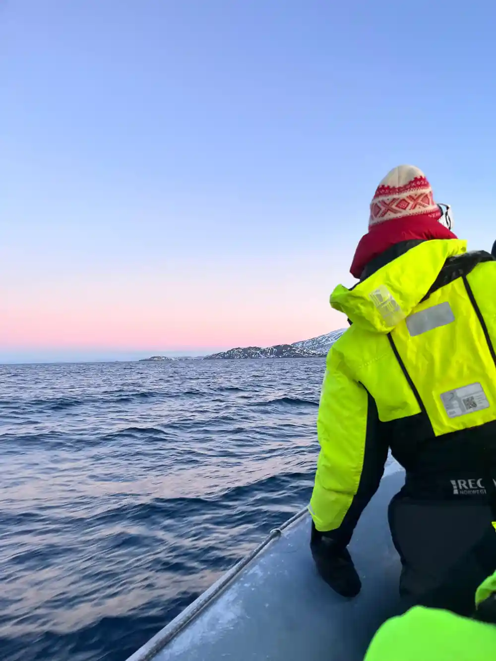 A passenger in a hi-vis flotation suit and woolly hat watching from the boat