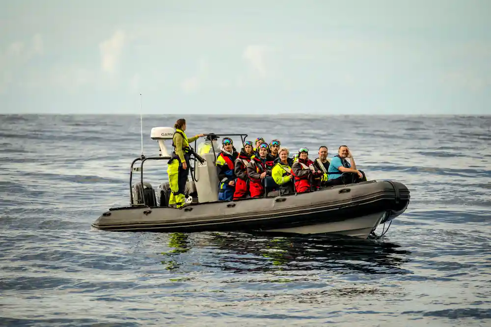 Passengers in coloured thermal suits packed onto an open RIB, helmsman standing