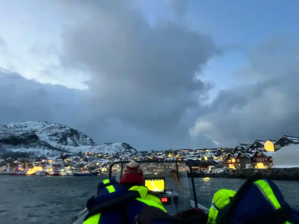 Passengers on the RIB looking towards a lit town under heavy cloud