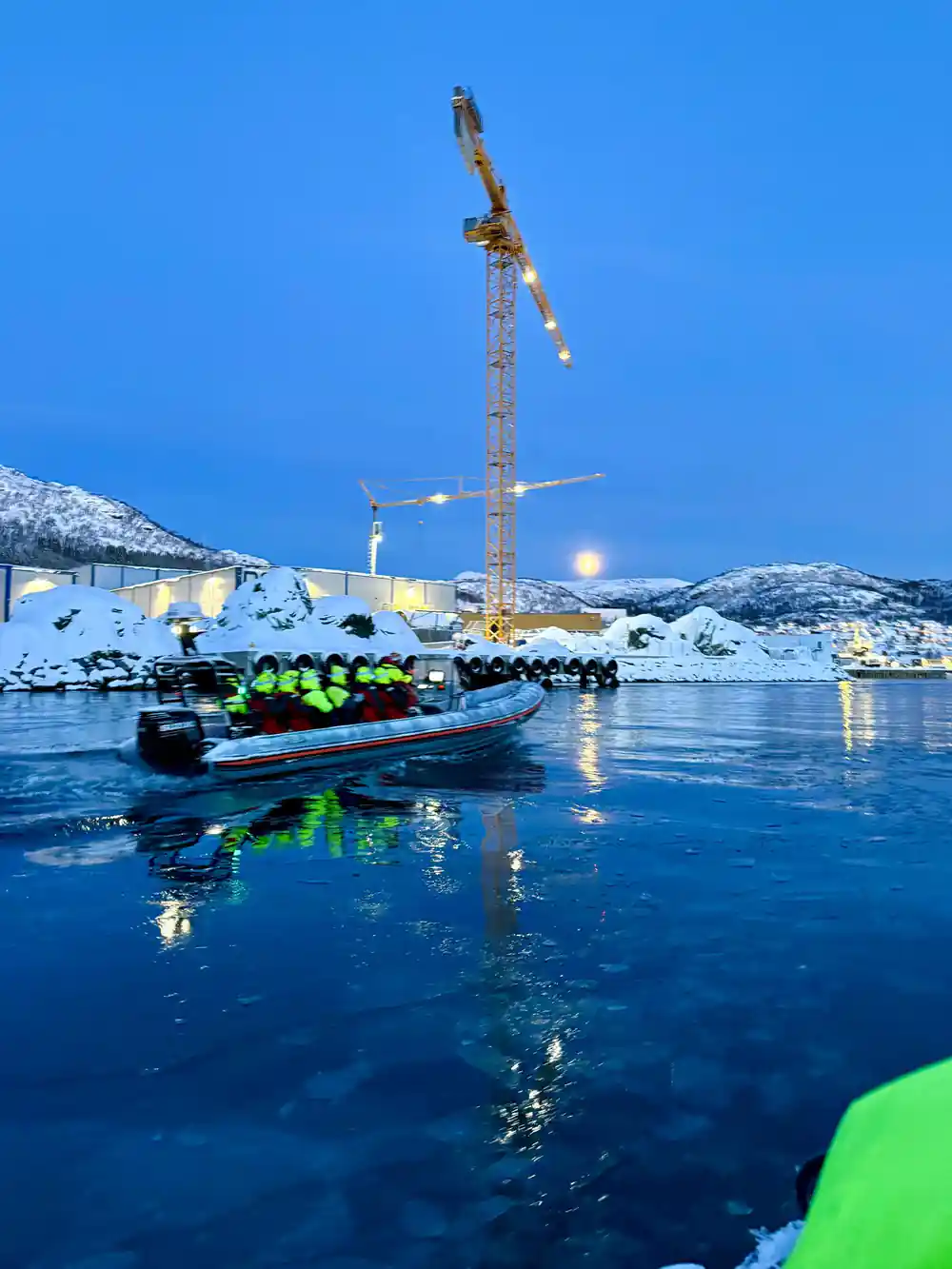 A RIB of passengers at a lit harbour under blue winter twilight